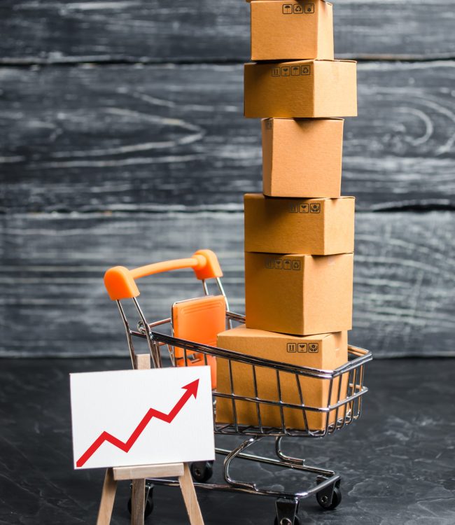 A supermarket cart loaded with lots of boxes and a red up arrow. The concept of increasing sales, increasing consumer ability and the welfare of society, consumer boom. Price increase and revenue.